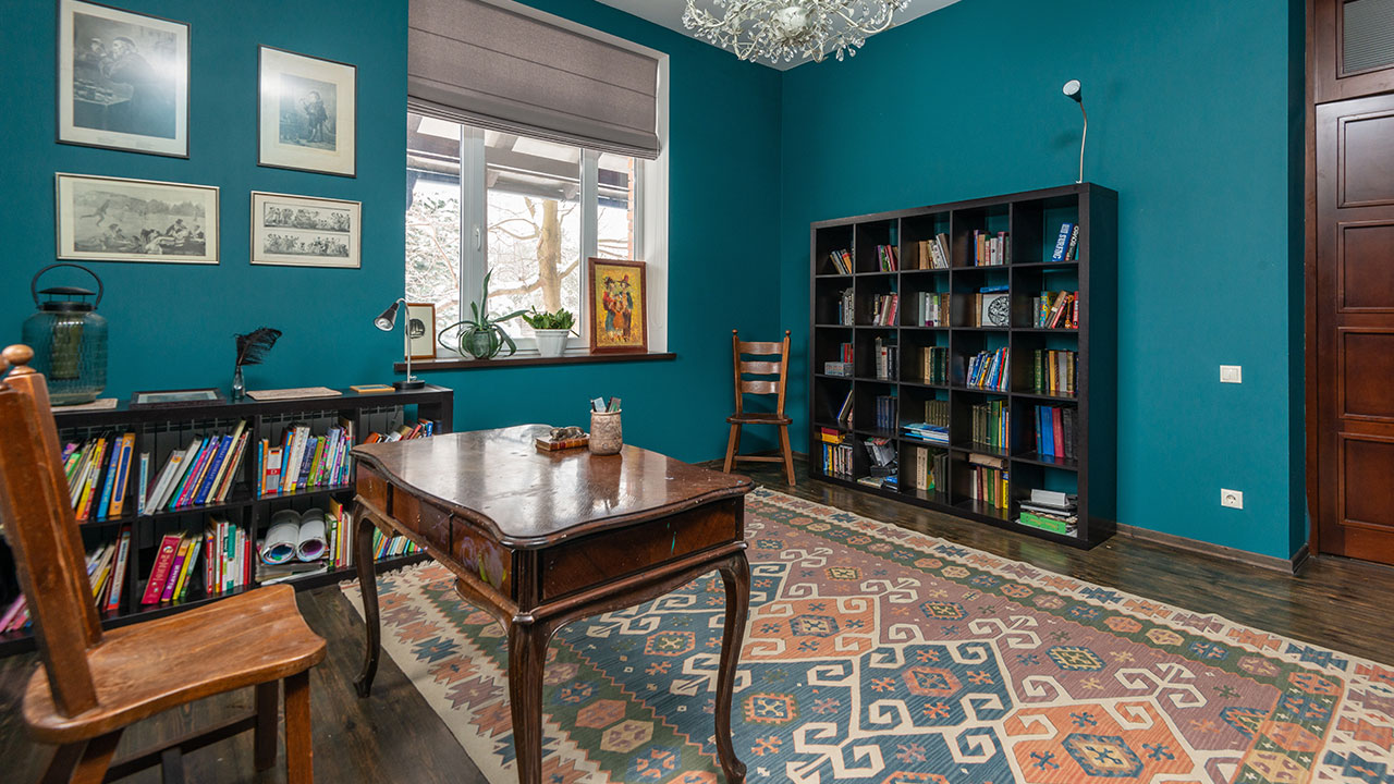 A study room with a wooden table a bookshelf and blue walls